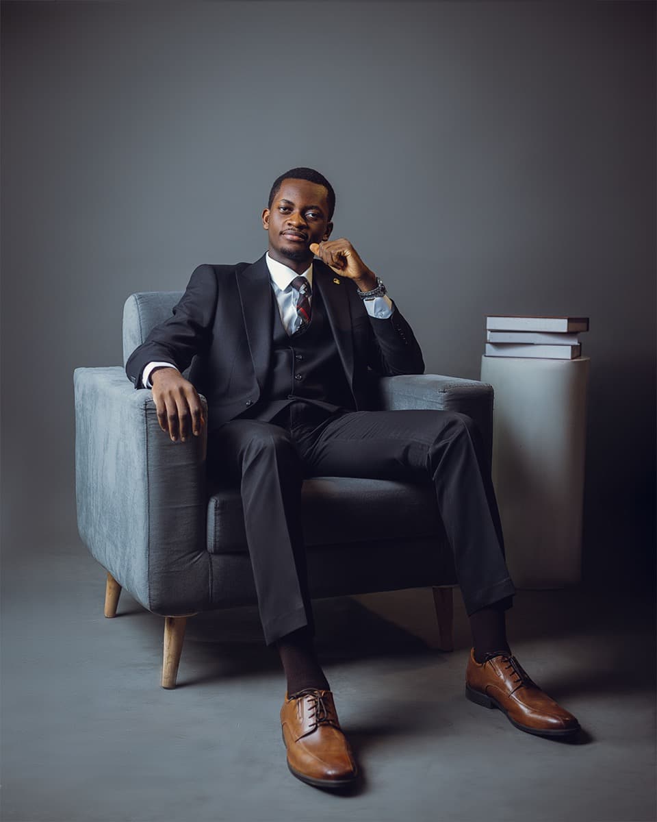 Ife Abimbola-Olulesi seated in an armchair beside a stack of books